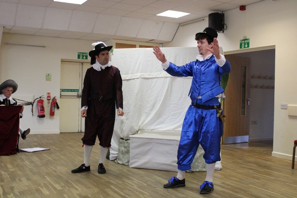 Two men in early modern costume, one with arms raised