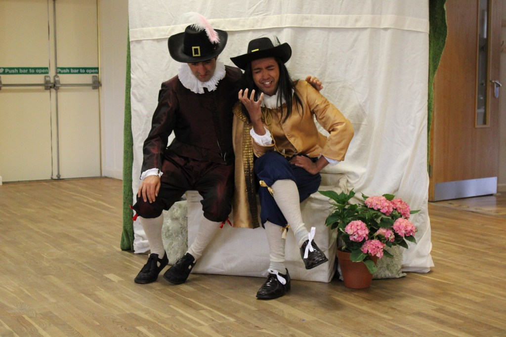 Two men sitting on a seat. One has his arm around the other