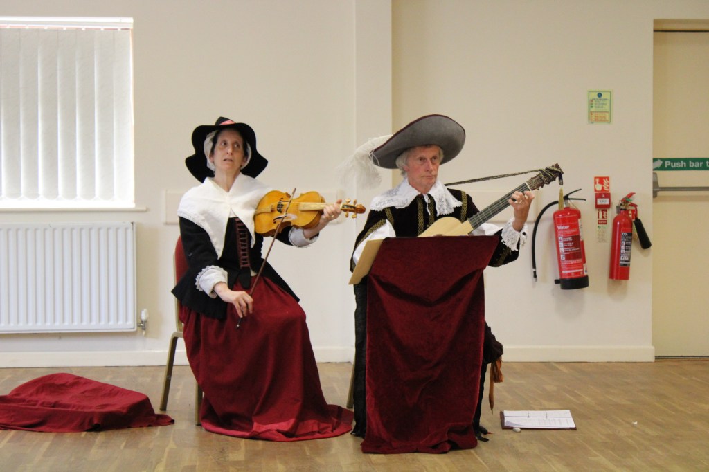 A woman playing a fiddle and a man playing a baroque guitar